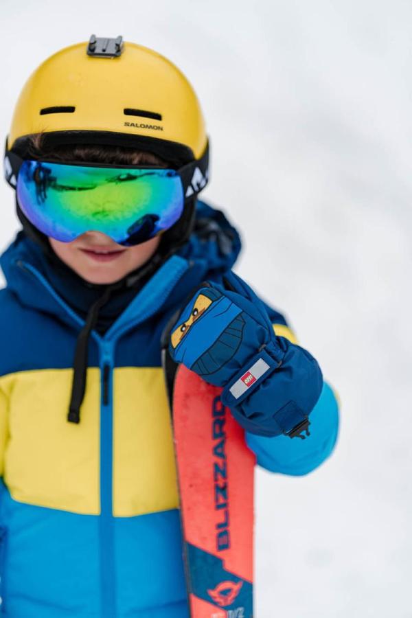 Kind in gelber und blauer Skijacke mit Helm und Skibrille.
