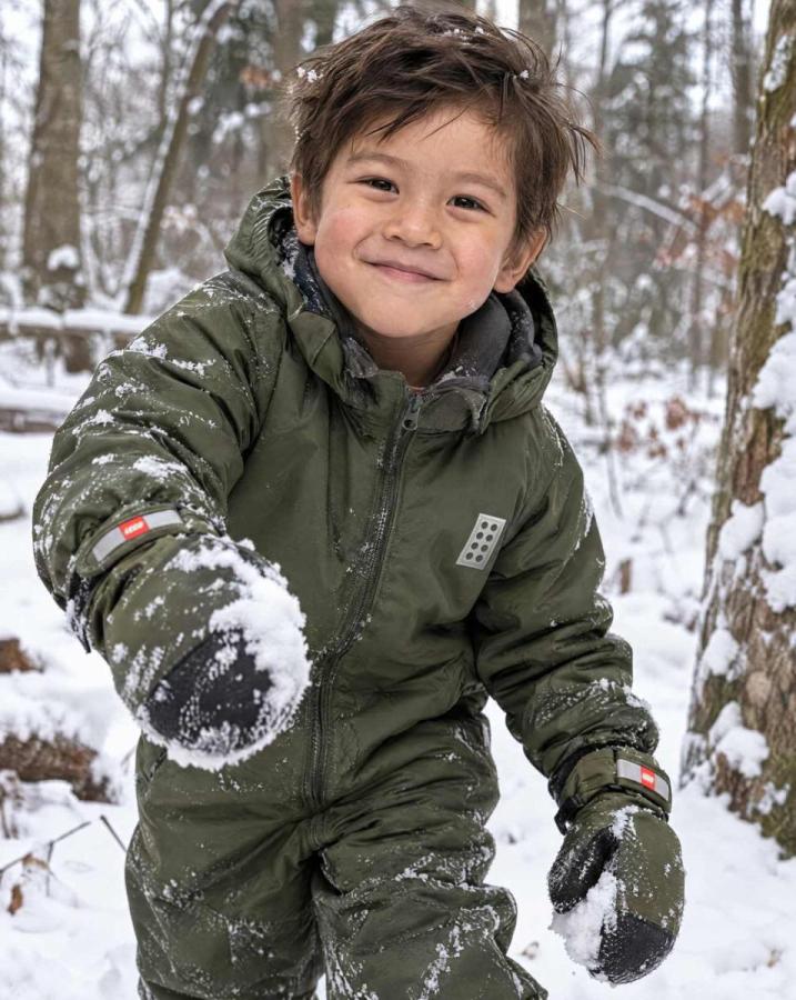 Kind im grünen Schneeanzug im Schnee.
