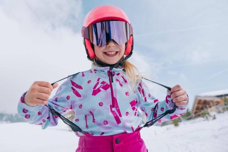 Kind zeigt die Kleidungsschicht unter einer Skijacke.
